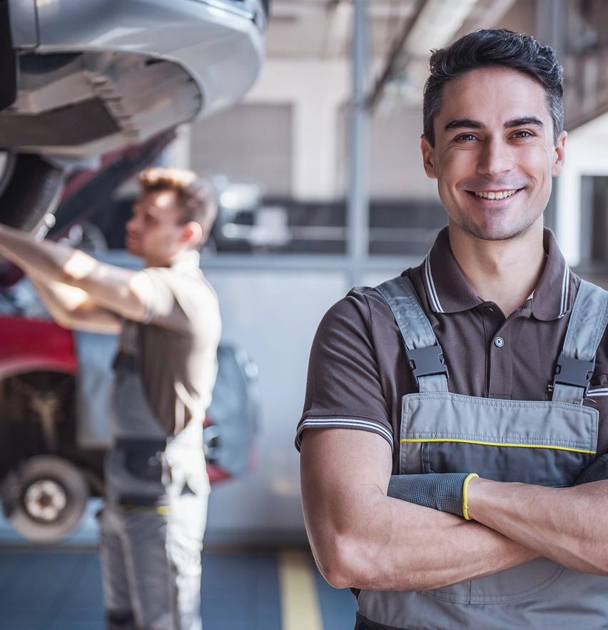 Araç servisinde arkada arabayla ilgilenen teknik servis uzmanı ve önde gülümseyerek bakan teknik servis uzmanı